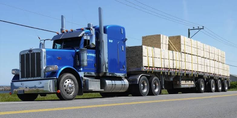 Semi-truck hauling a loaded flatbed trailer on the highway